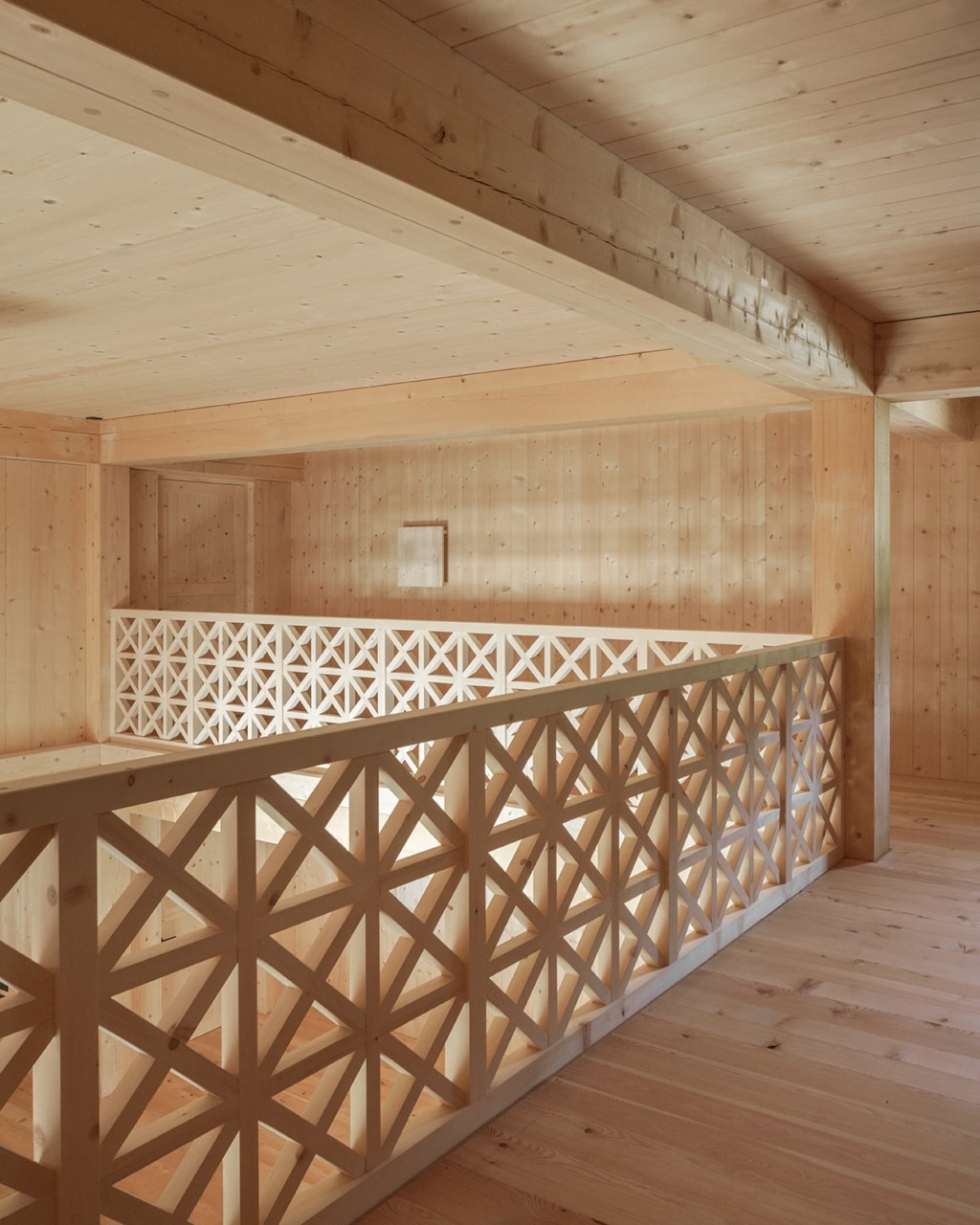Una zona a galleria aperta realizzata in legno, caratterizzata da un'atmosfera tranquilla e dalle linee pulite: pareti, soffitti e pavimento sono interamente in legno e ne esaltano il carattere caldo e naturale. Una ringhiera delicata dal motivo geometrico delimita l'apertura sul piano sottostante e conferisce all'ambiente un aspetto artigianale e allo stesso tempo leggero.