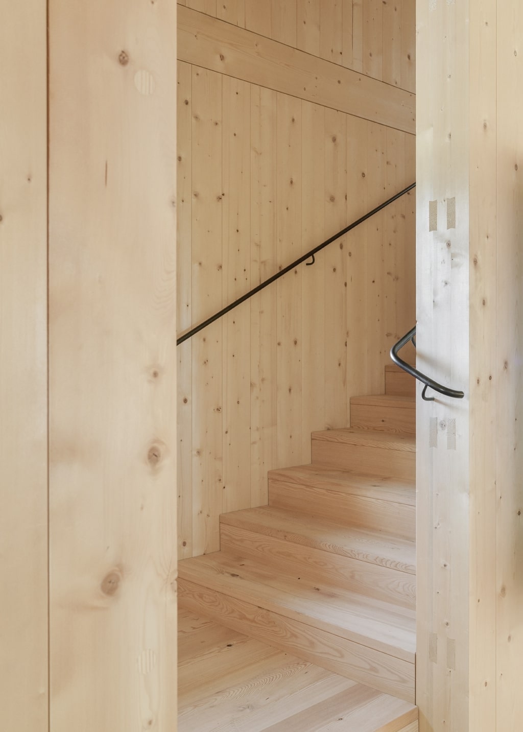 Una scala dal design compatto, realizzata in legno con uno stile pulito ed essenziale: pareti, gradini ed elementi portanti sono interamente in legno chiaro e presentano giunti a vista. Un sottile corrimano in metallo accompagna la scala, creando un delicato contrasto con il carattere caldo del materiale.