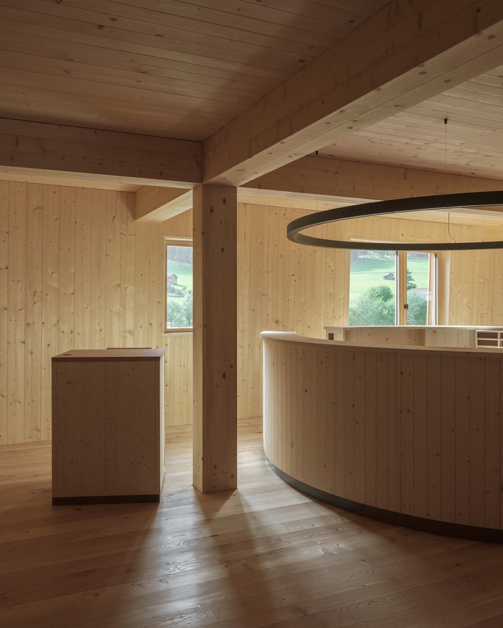 Un ambiente interno accogliente, interamente realizzato in legno, dall'atmosfera sobria e tranquilla: al centro della sala spicca un bancone circolare rivestito in legno, messo in risalto da una lampada sospesa a forma di anello. Pilastri e travi in legno massiccio definiscono lo spazio, mentre le finestre offrono scorci suggestivi sul paesaggio alpino e lasciano entrare delicatamente la luce naturale.