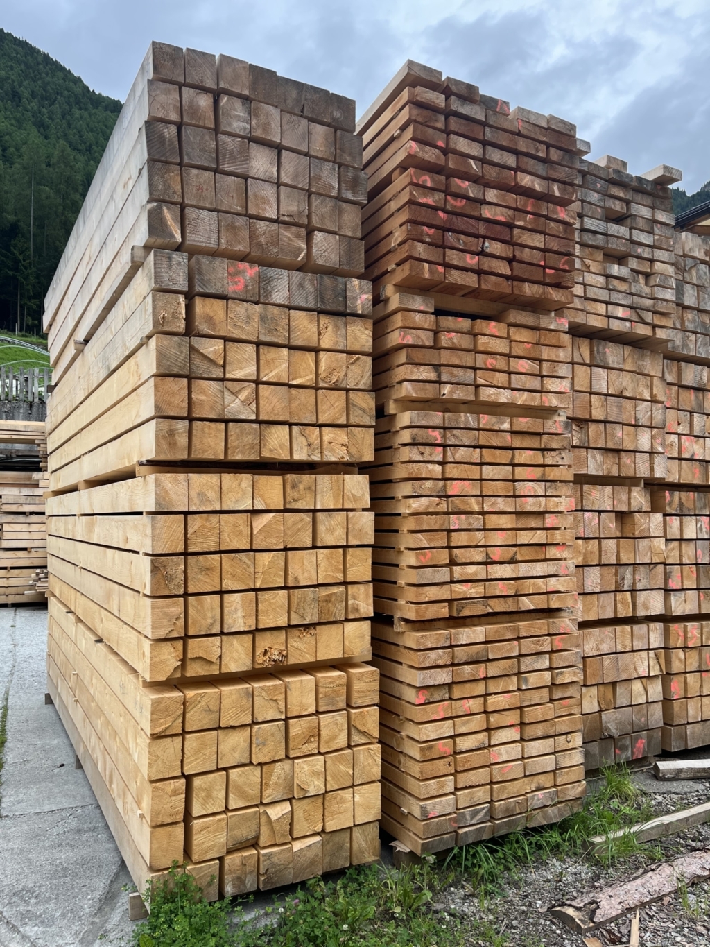 Travi in legno massello al naturale accatastate nel deposito esterno, impilate con cura e pronte per la lavorazione successiva.