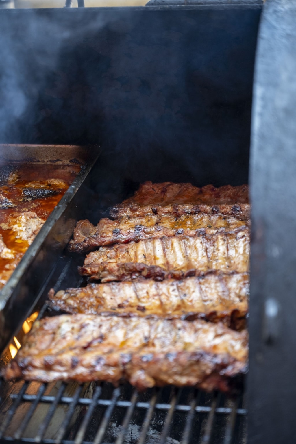 Spareribs die auf einem Smoker liegen. Darunter brennt ein kleines Feuer.