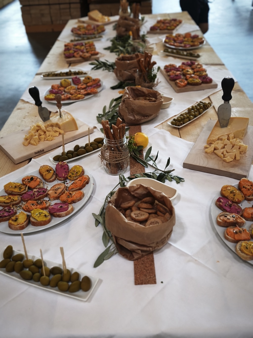 Buffet auf einem Holzstapel mit Brötchen, Käse, Oliven und Grissini.