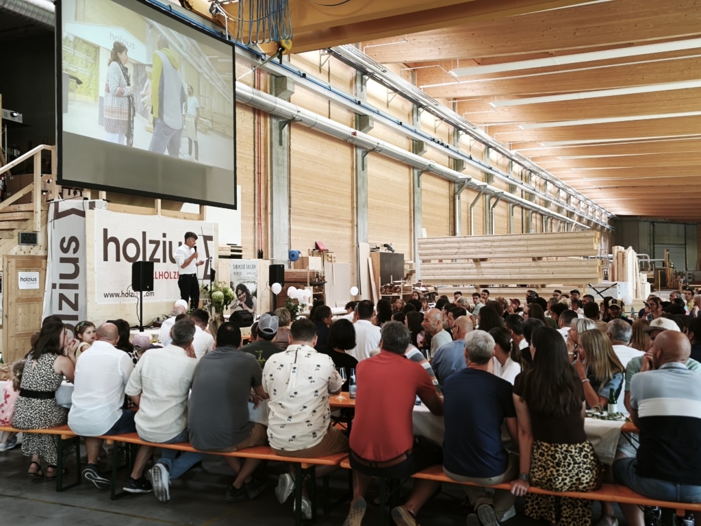 BesucherInnen genießen und unterhalten sich auf der 100-Jahre-Rubner-Feier in der holzius Heimstatt, umgeben von Vollholz.