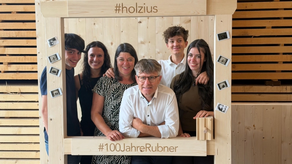 Familie Niederfriniger hinter einem Bilderrahmen aus Holz mit der Aufschrift #holzius und #100JahreRubner.